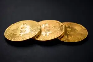 three gold-colored bitcoins on black surface